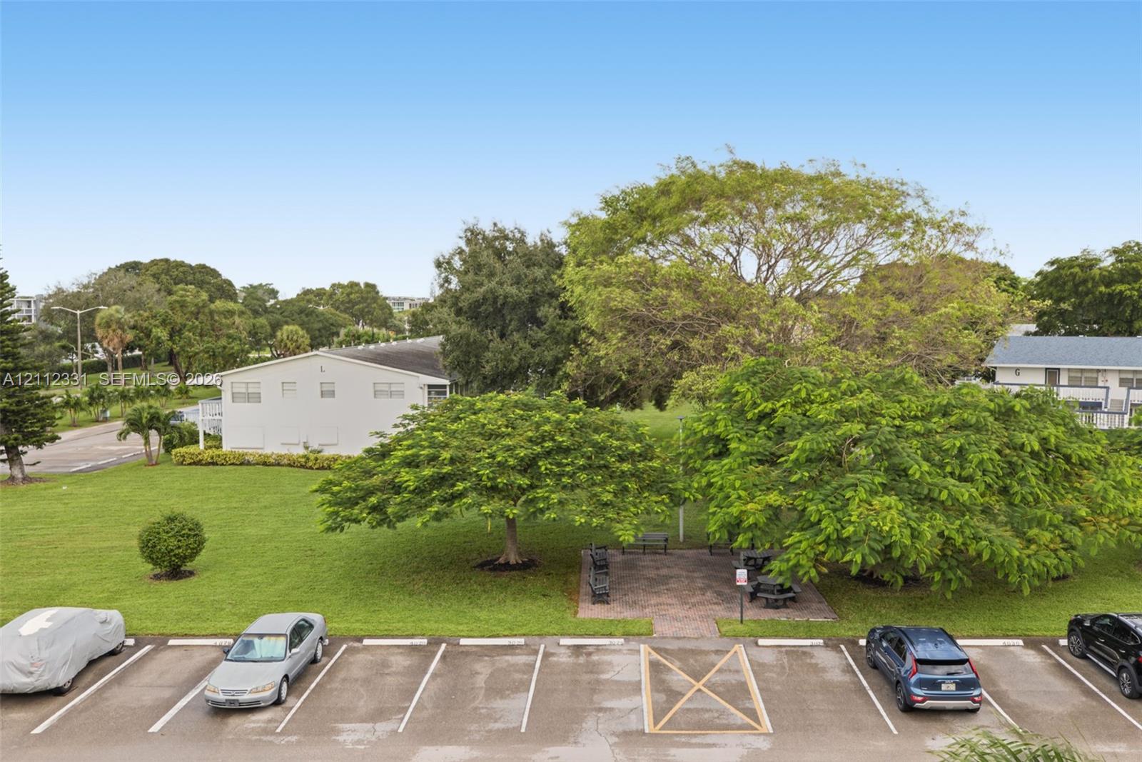 Expansive grounds featuring a manicured lawn, mature shade trees, and a paved common area