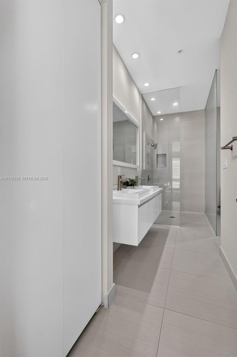 Floating white vanity with dual vessel sinks, recessed lighting, and a walk-in shower featuring a glass enclosure and recessed shelving