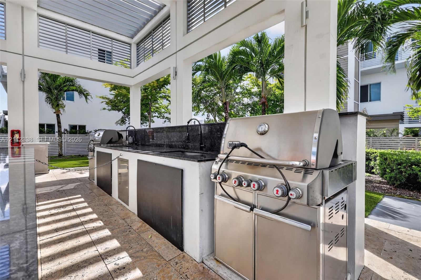 Covered outdoor kitchen featuring a stainless steel grill, stone countertop, built-in sink, and stone-tile flooring