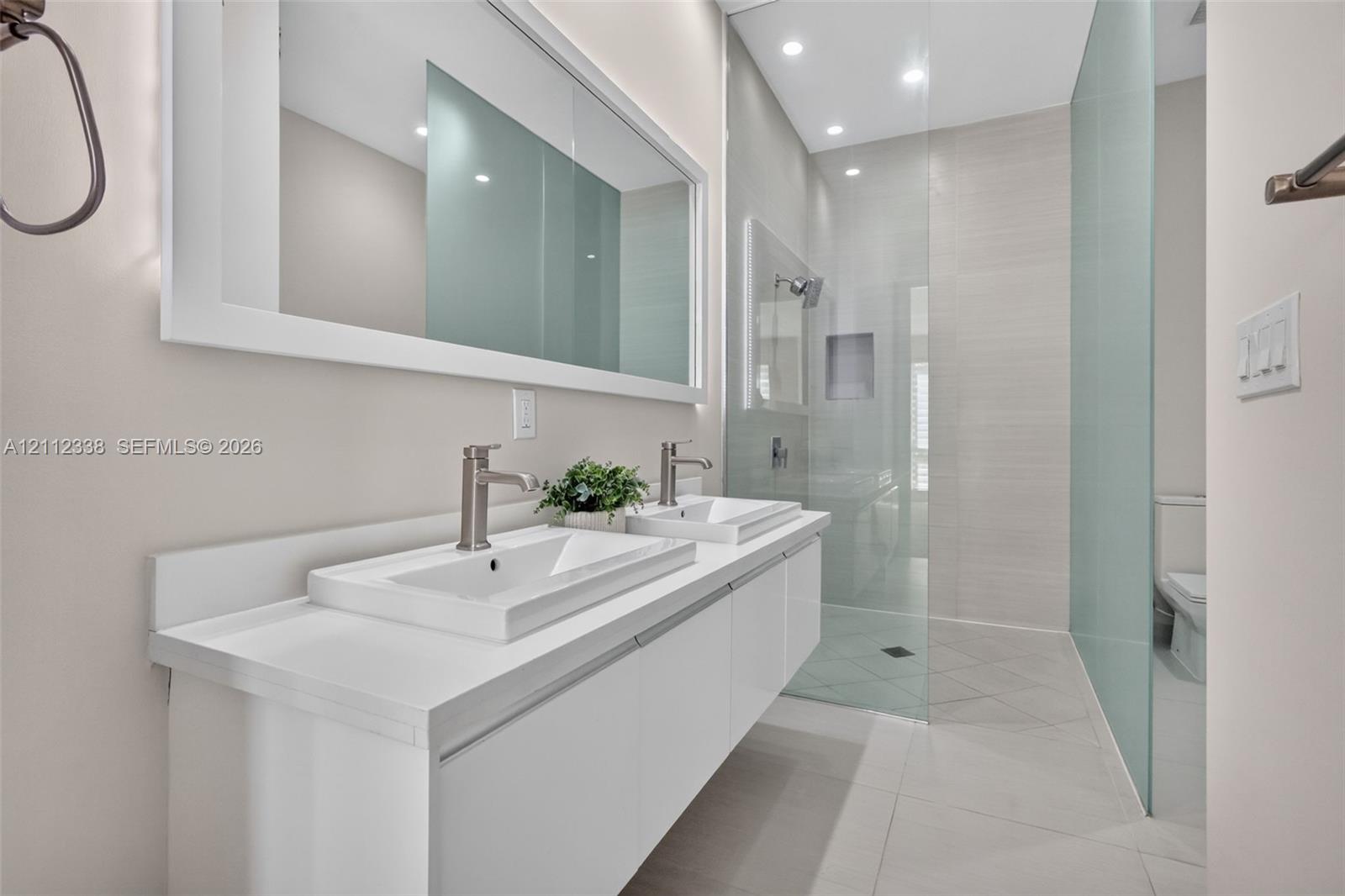 Double floating vanity with rectangular sinks, integrated mirror, glass-enclosed shower featuring a recessed niche, and stone-finish floor tiling