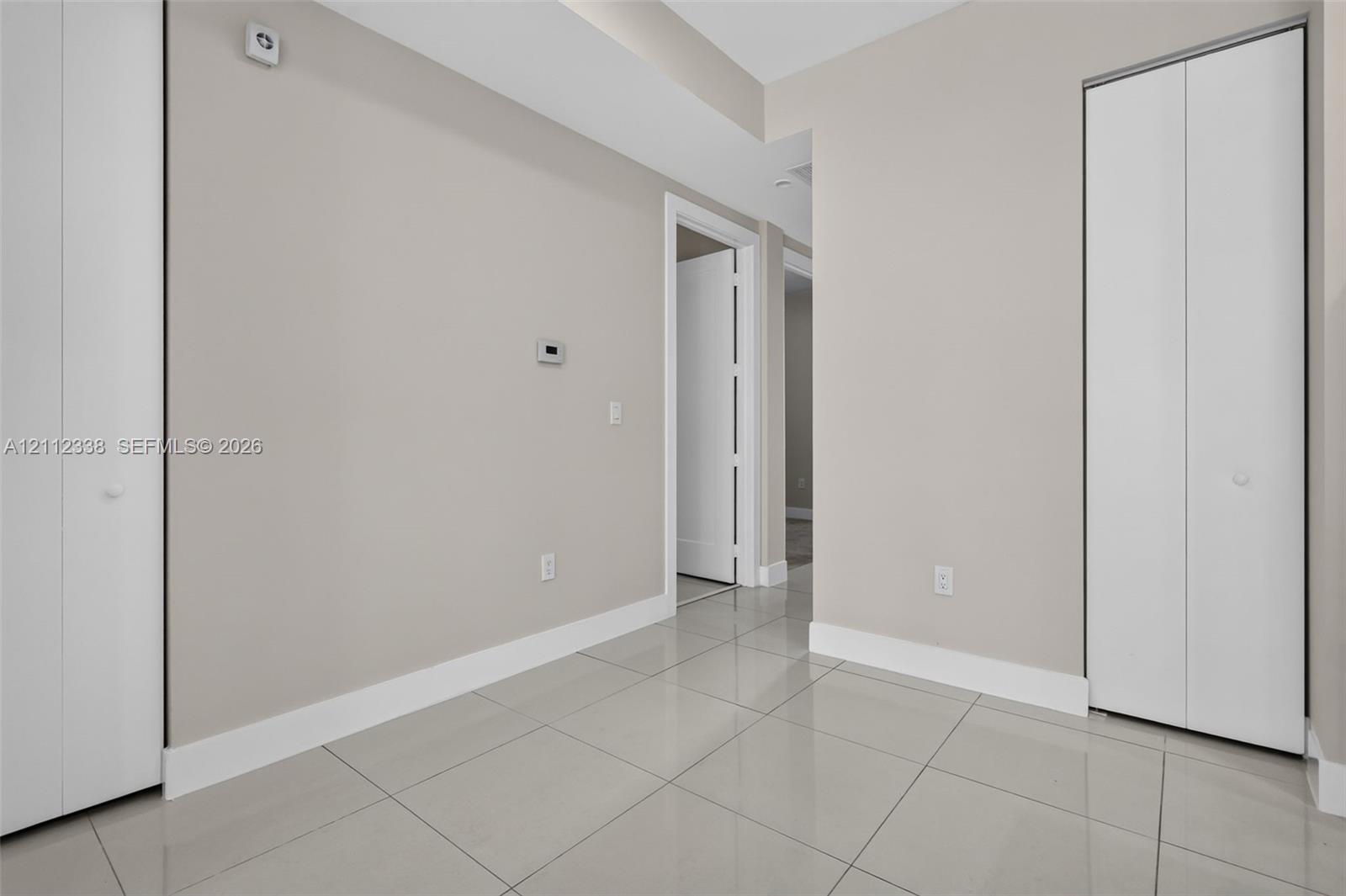 Interior space featuring large-format neutral tile flooring, two sets of white bi-fold closet doors, and smooth wall finishes