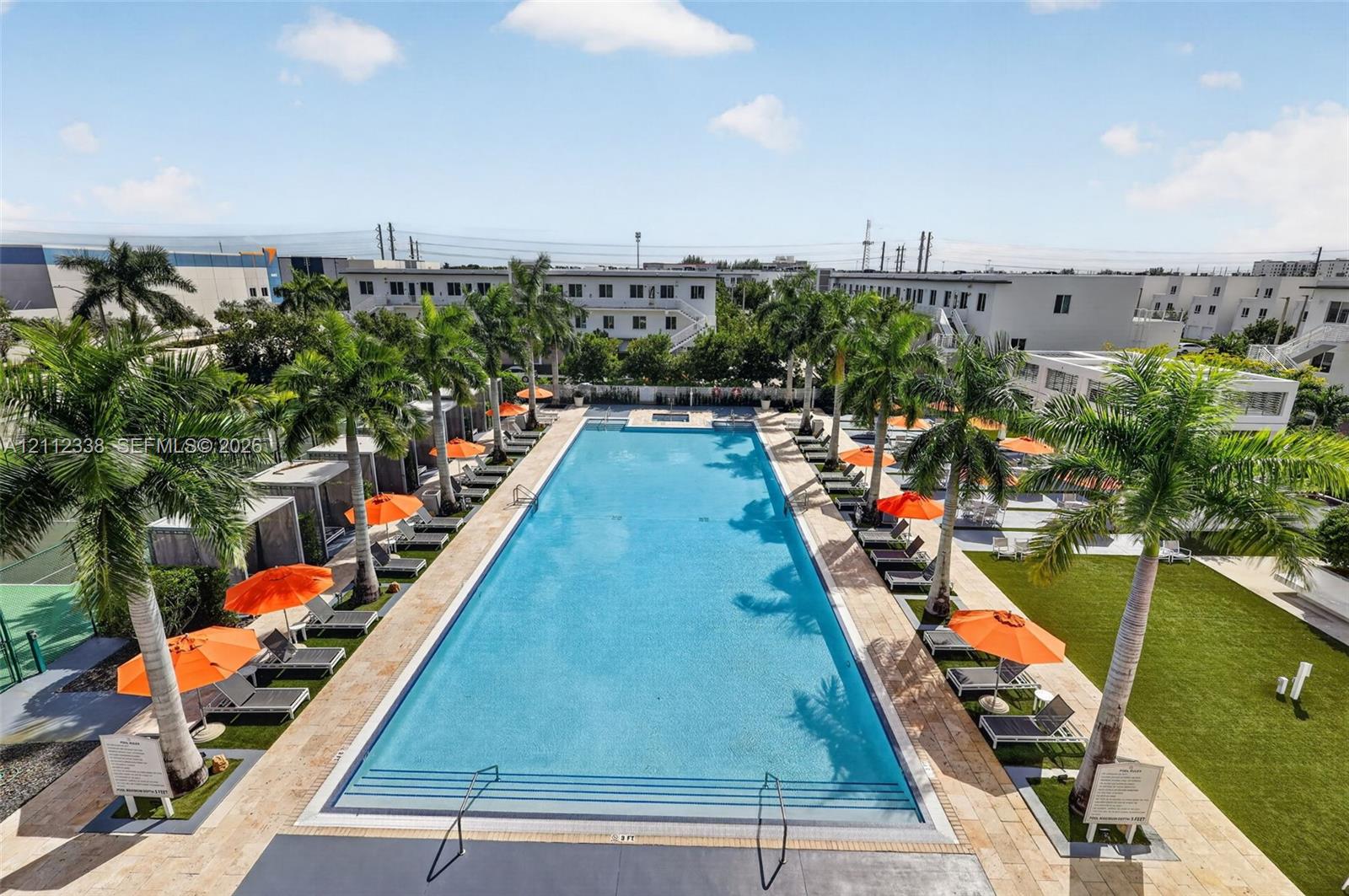 Rectangular swimming pool featuring a stone-tile deck, integrated stairs, perimeter palm trees, and artificial turf lawn space