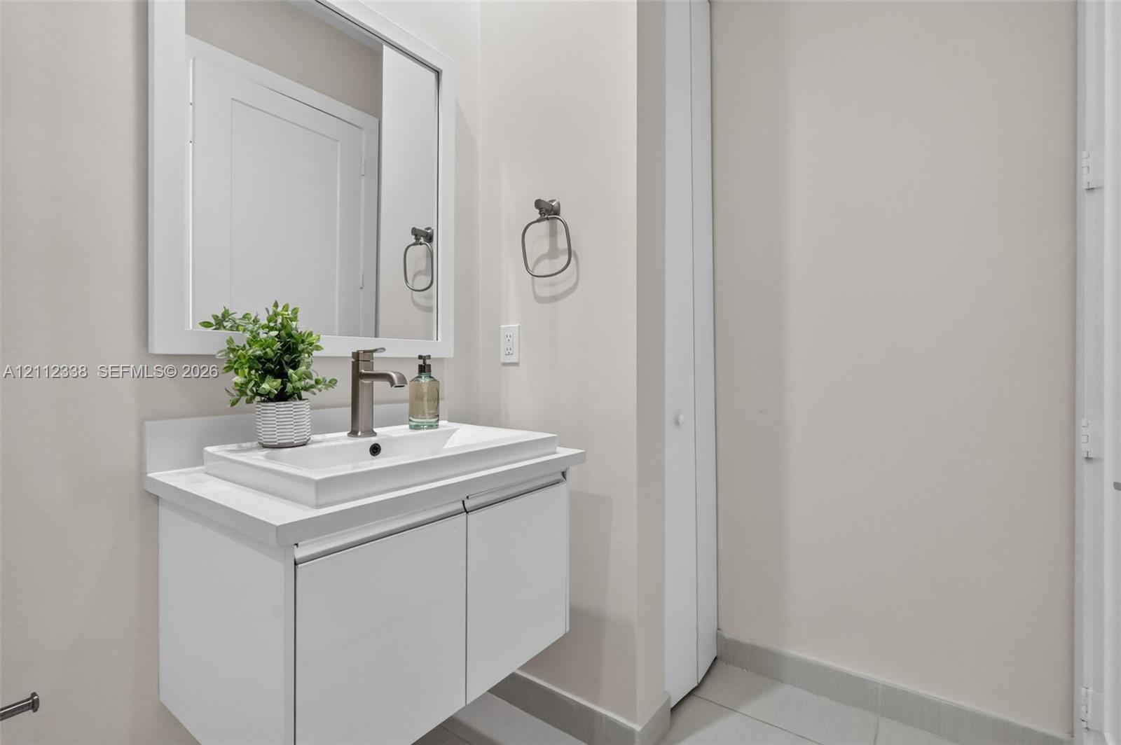 Floating vanity featuring a white cabinetry finish, rectangular vessel sink, brushed metal faucet, and framed wall mirror