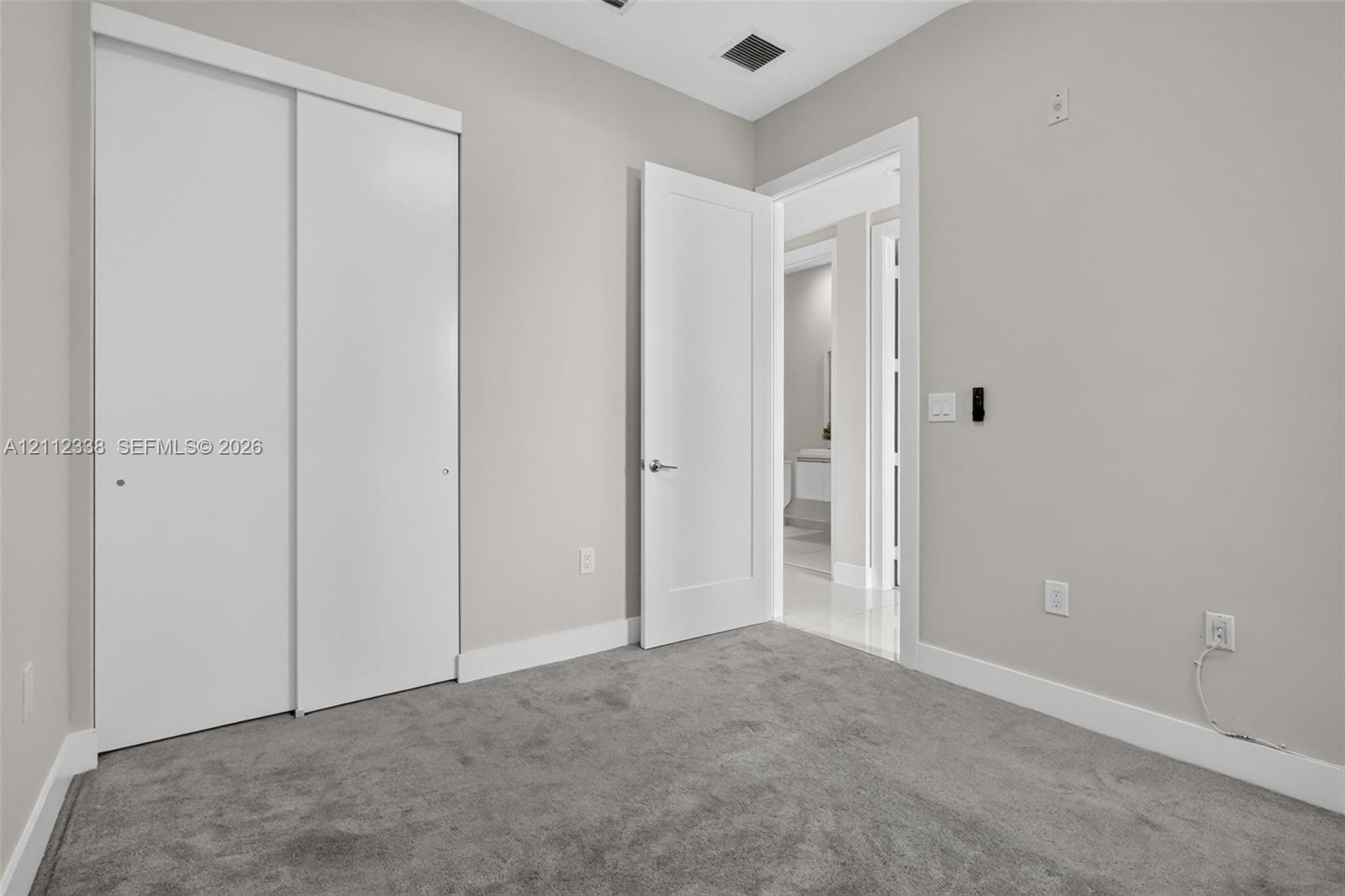 Room featuring neutral wall tones, plush wall-to-wall carpeting, white sliding closet doors, and a solid-core hinged interior door