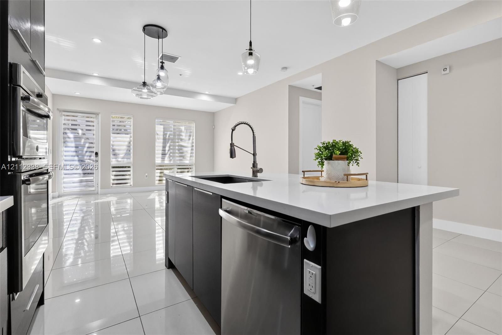 Kitchen island featuring a stone-surface countertop, dark cabinetry, an undermount sink, a pull-down faucet, and a stainless steel dishwasher