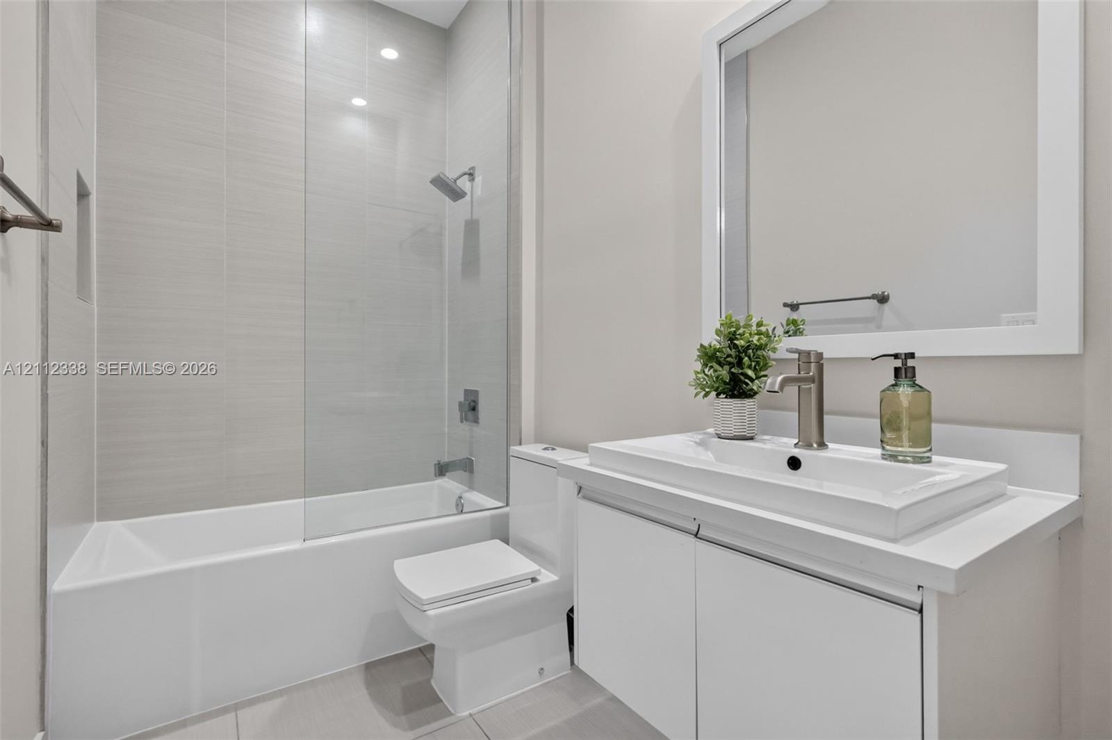 Full bathroom featuring a white vanity with a rectangular vessel sink, solid surface countertop, glass shower panel, and light-toned wall tile
