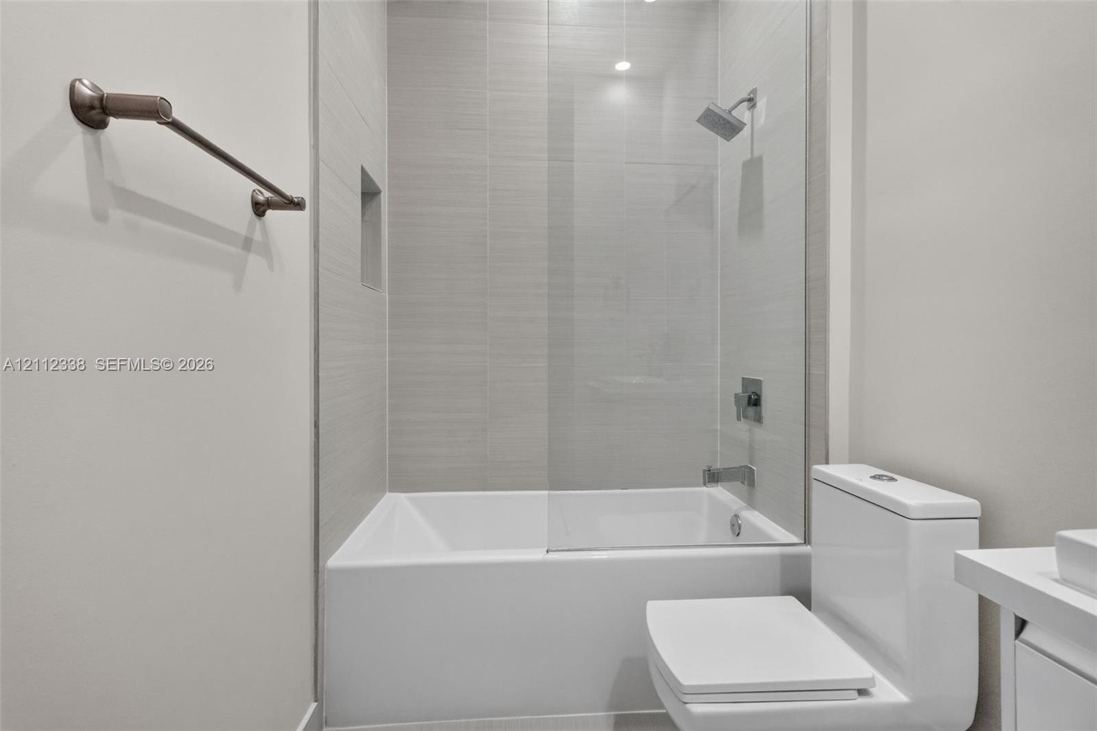 Full-height tile surround with a recessed niche, frameless glass shower panel, and wall-mounted shower fixture