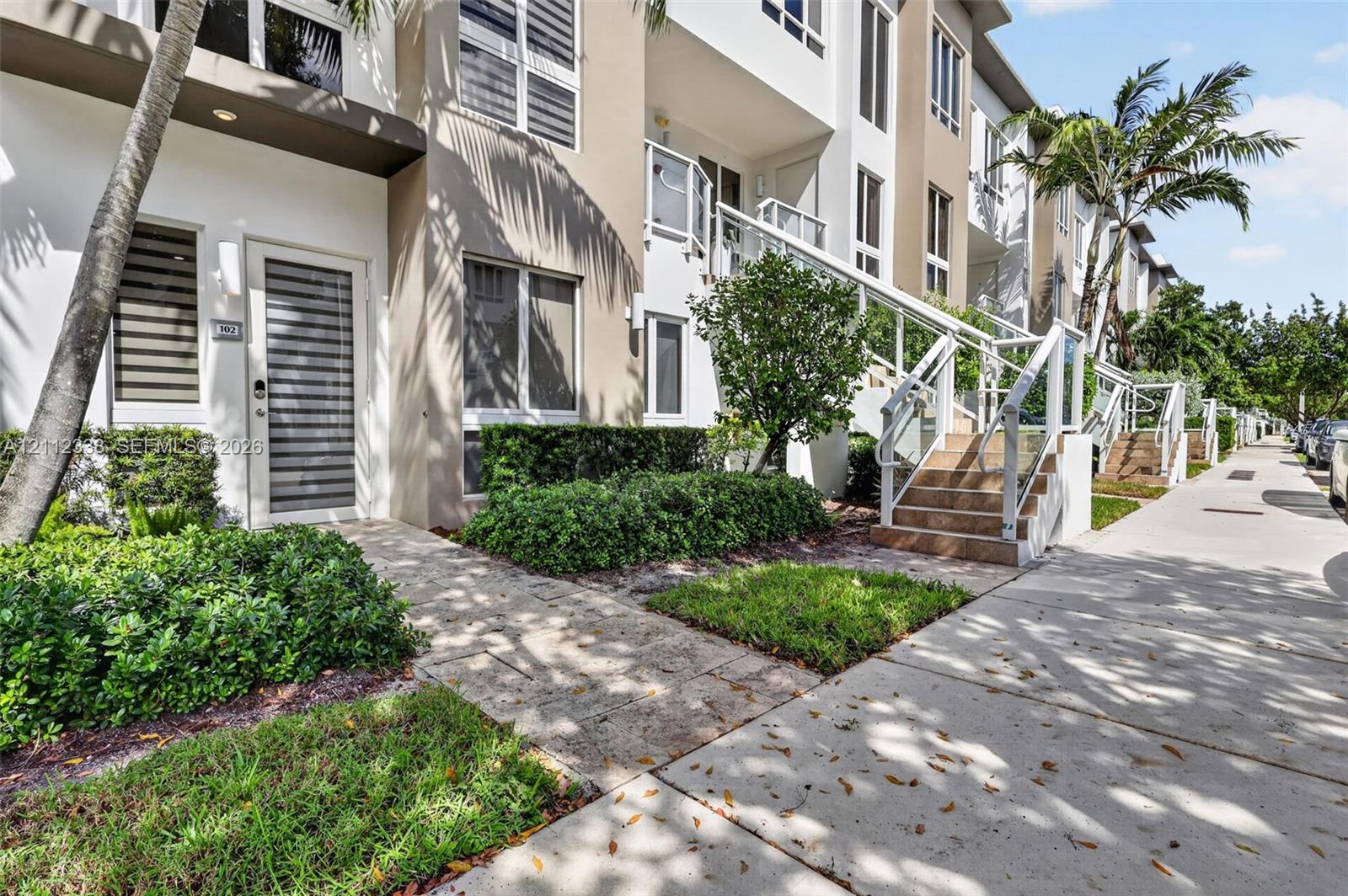 Multi-level exterior featuring a smooth stucco facade, elevated concrete staircase with glass railings, stone-paver walkways, and manicured landscaping