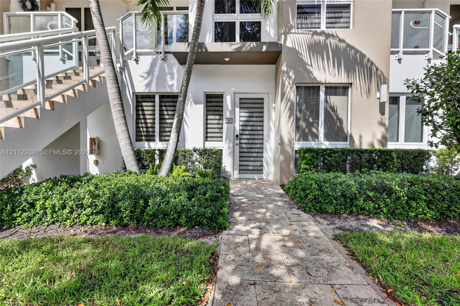 Exterior featuring a stone paver walkway, multi-pane windows with horizontal blinds, glass-panel stair railing, and a private entrance with a horizontal-slat door