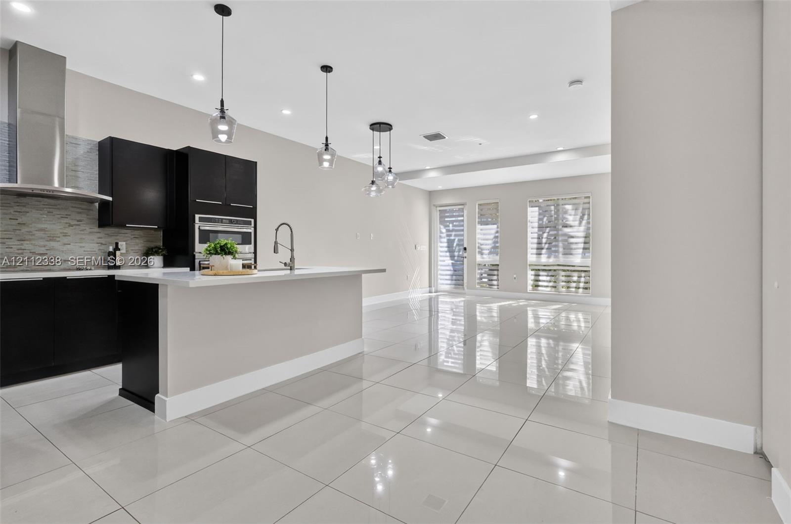 Modern kitchen featuring high-gloss cabinetry, a central island with a solid surface countertop, stainless steel appliances, polished tile flooring, and glass pendant lighting