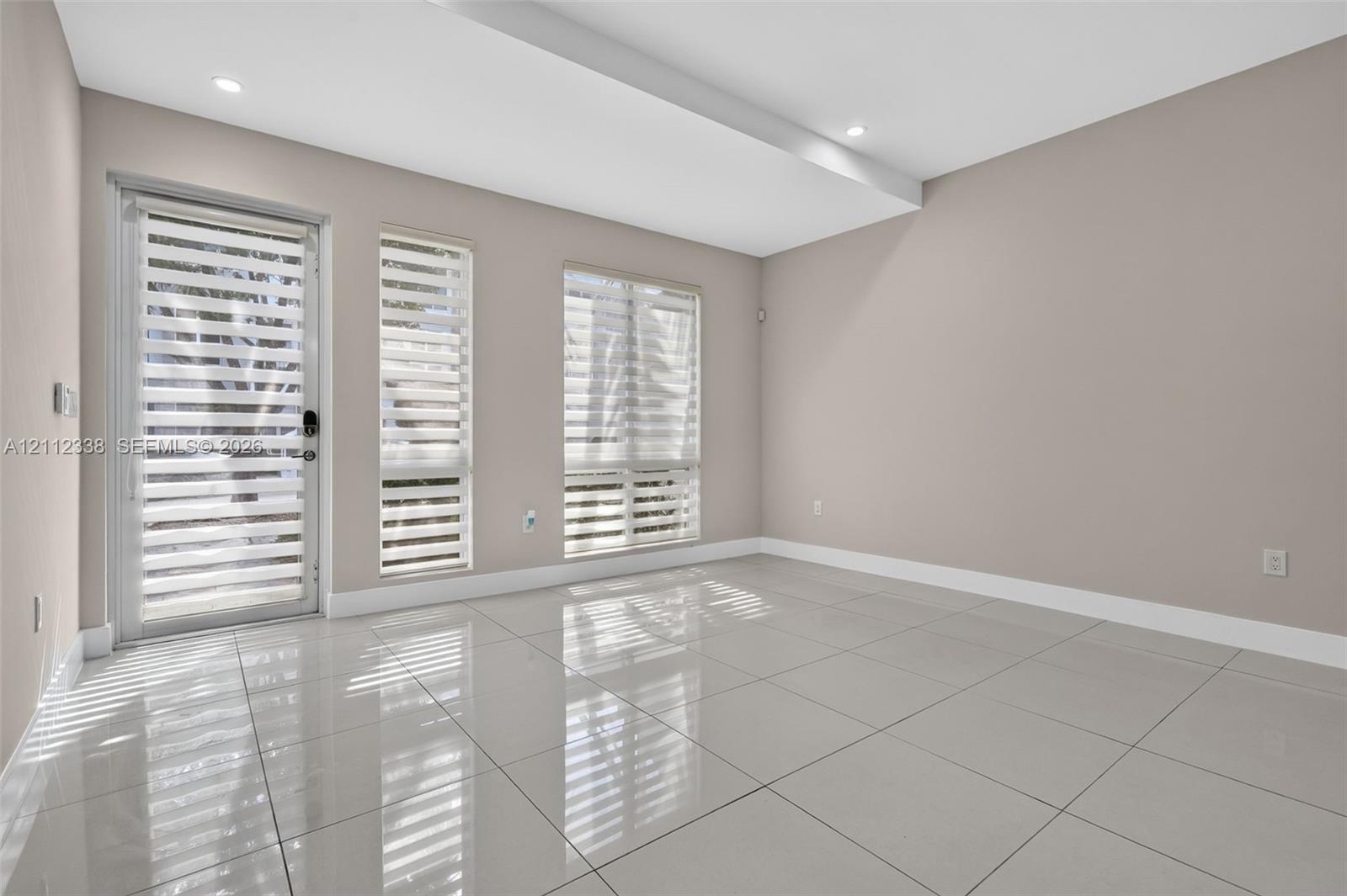 Neutral-toned interior featuring large-format polished tile flooring, recessed ceiling lighting, a glass-panel exterior door, and multiple windows with adjustable roller shades Neutral-toned interior featuring large-format polished tile flooring, recessed ceiling lighting, a glass-panel exterior door, and multiple windows with adjustable roller shades