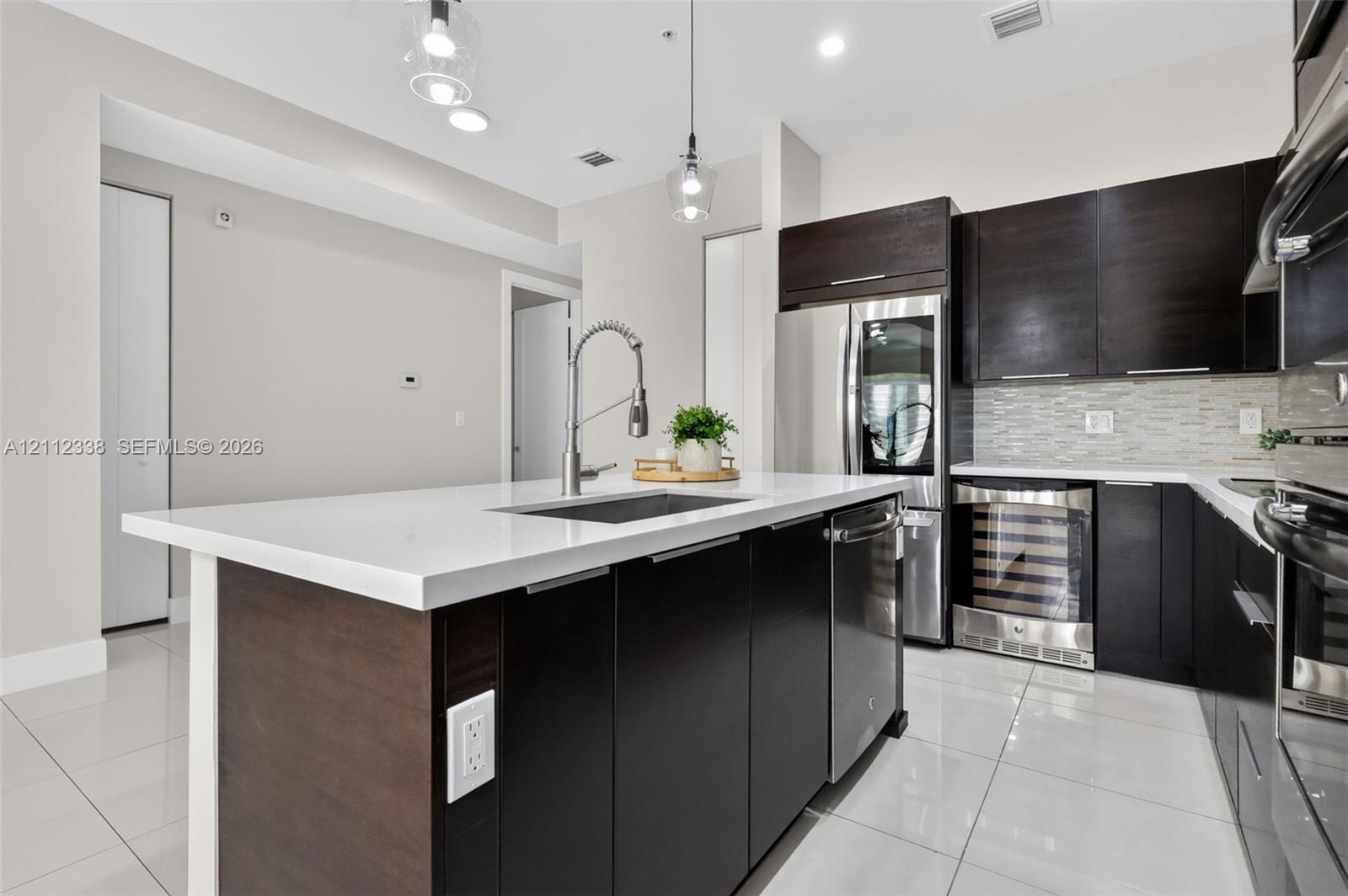 Kitchen featuring a central island with a solid surface countertop, dark-finish cabinetry, stainless steel appliances, a built-in wine refrigerator, and polished floor tile