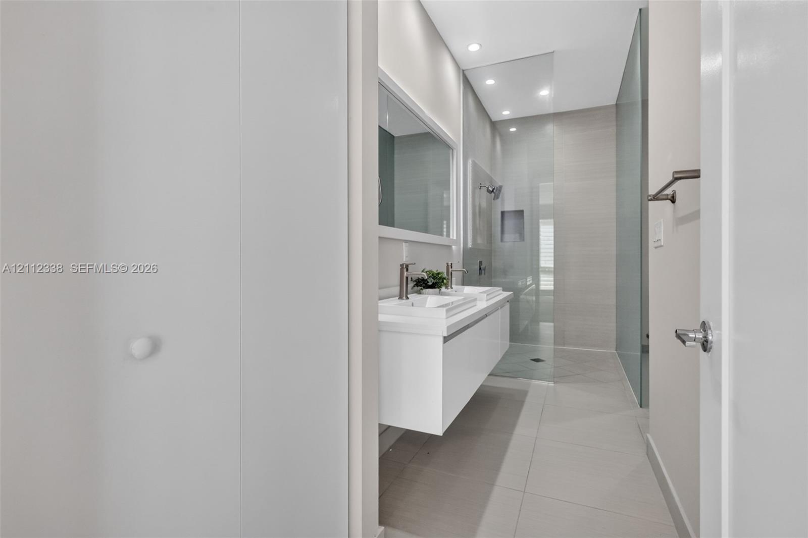 Modern floating dual vanity with integrated sinks, recessed lighting, large-format tile flooring, and a walk-in shower enclosed by a seamless glass panel