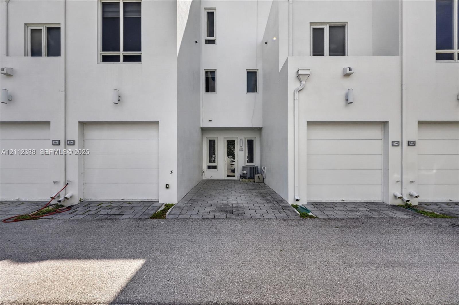 Modern exterior featuring multi-level white stucco facade, paved driveway, and multiple integrated garage bays with overhead doors