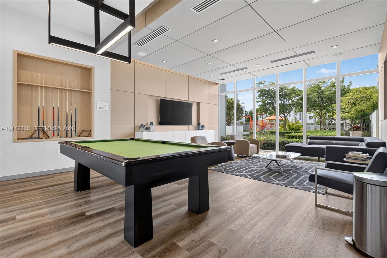 Common area featuring floor-to-ceiling windows, wood-finish flooring, custom wood-panel wall treatments, integrated recessed lighting, and a modern geometric pendant fixture