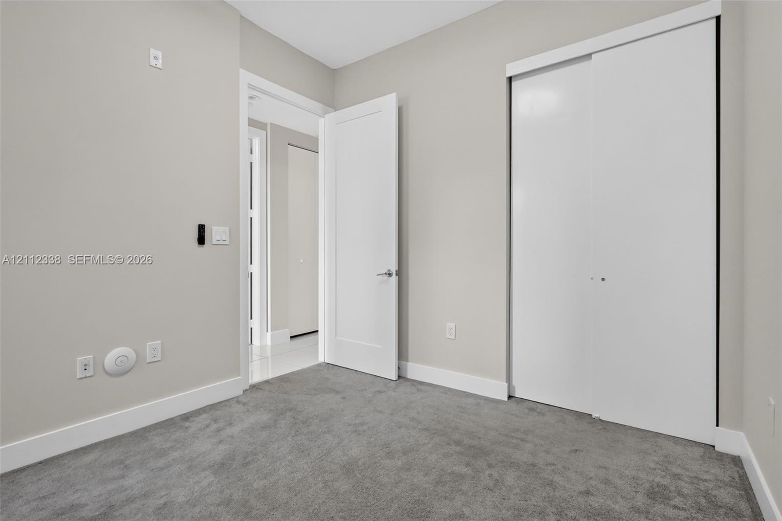Interior space featuring plush neutral carpeting, smooth-finish walls, a solid-core swing door with brushed metal hardware, and a sliding-panel closet with white finishes