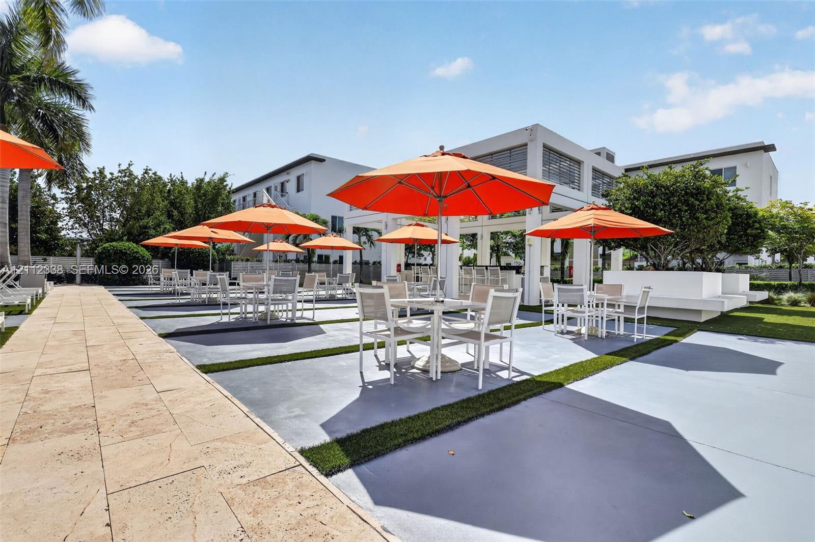 Outdoor recreation area featuring a paved stone walkway, hardscaped patio surface with synthetic grass inlays, and an open-air covered pavilion