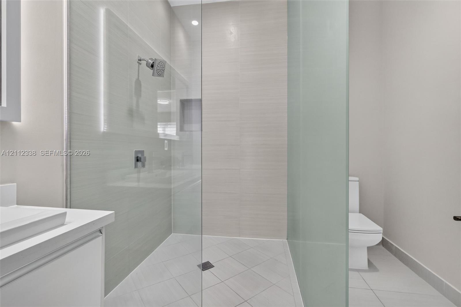 Walk-in shower featuring glass enclosure, wall-mounted shower head, recessed shelving, and tiled flooring