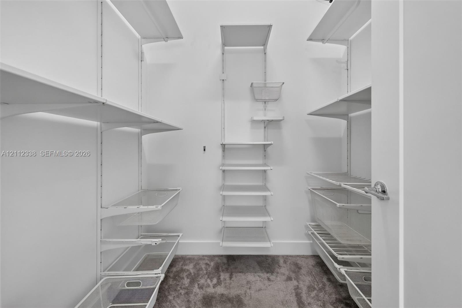 Storage space featuring a customizable white wire shelving system with multiple tiered racks and integrated slide-out wire baskets, complete with wall-to-wall carpeting