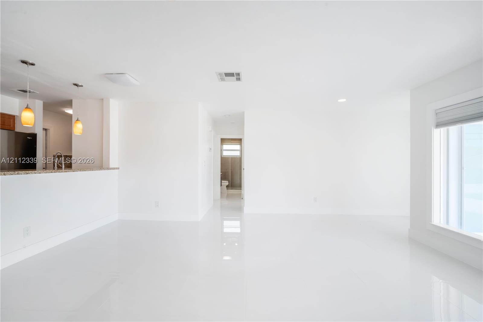 Open-concept interior featuring high-gloss tile flooring, recessed ceiling lighting, a kitchen peninsula with a stone-finish countertop, and two pendant light fixtures