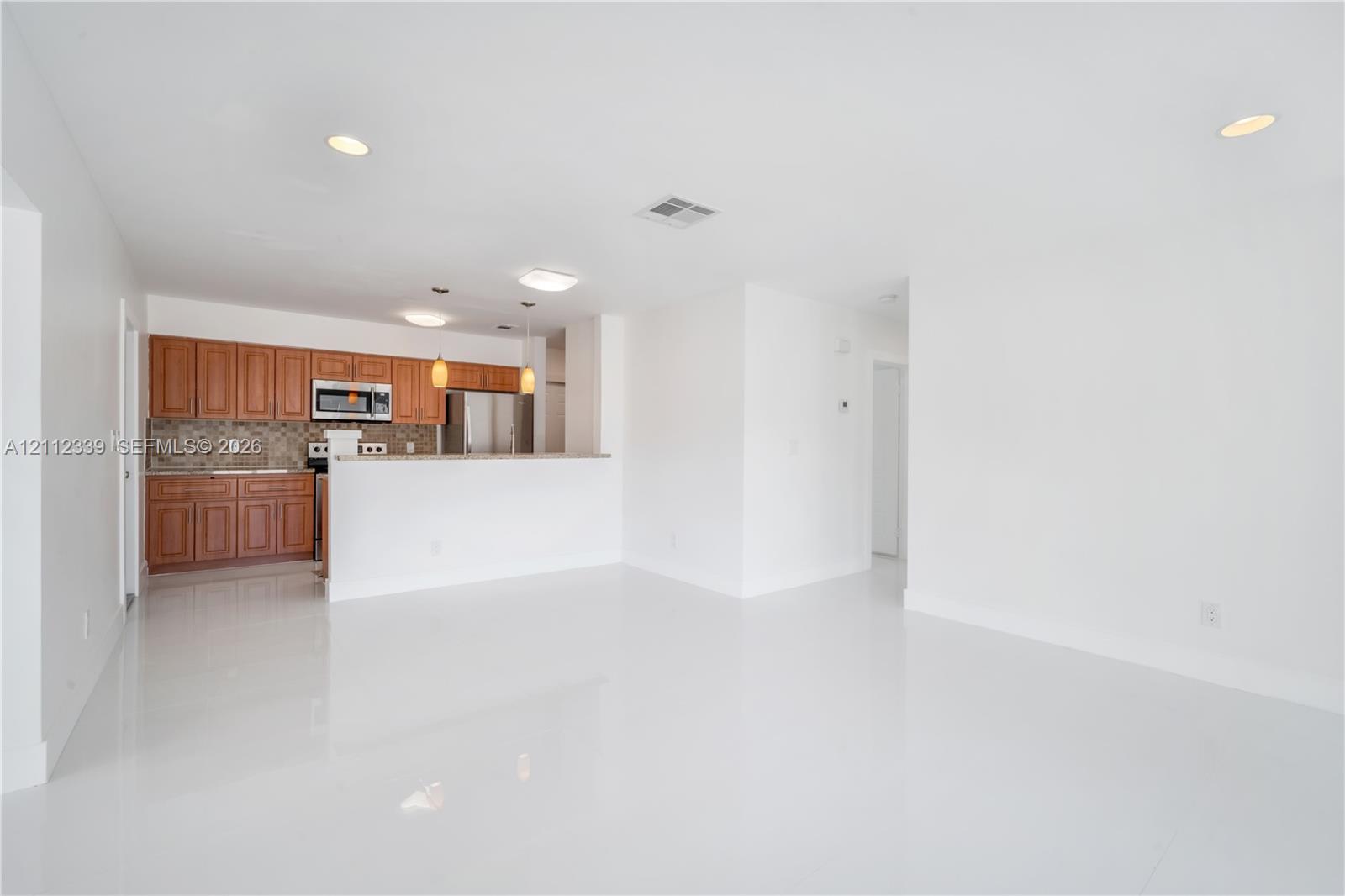 Kitchen area featuring wood cabinetry, stone-tiled backsplash, breakfast bar with a granite countertop, tiled backsplash , recessed lighting, and white tile flooring throughout