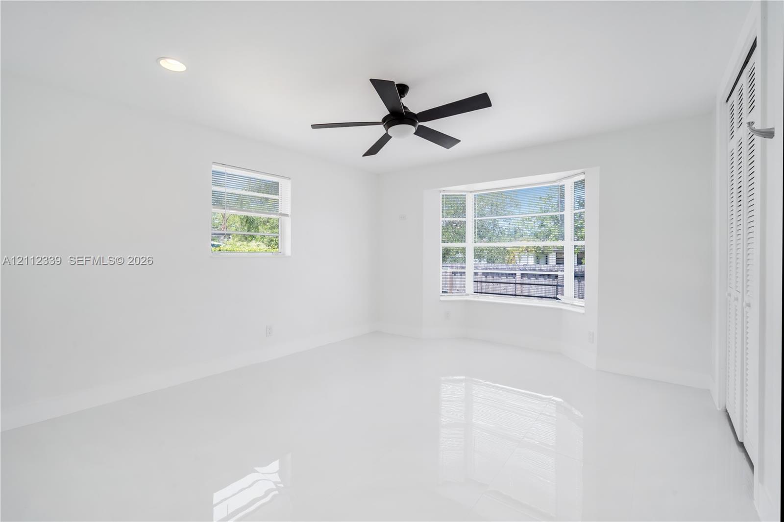 Bright interior featuring polished tile flooring, a bay window, recessed lighting, a ceiling fan, and louvered closet doors
