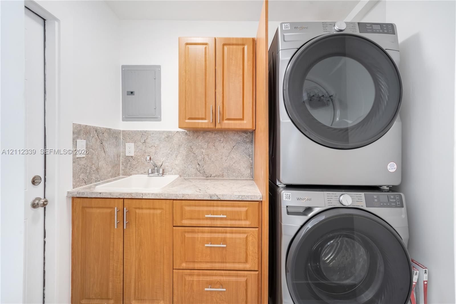 Laundry area featuring wooden cabinetry, a built-in utility sink, and stacked full sixed laundry appliances * Door on the left leads to the backyard *