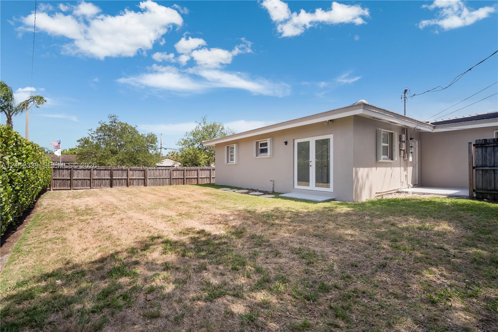 Private backyard featuring a privacy hedge, wood-panel fencing, and exterior French doors leading to one of the bedrooms *