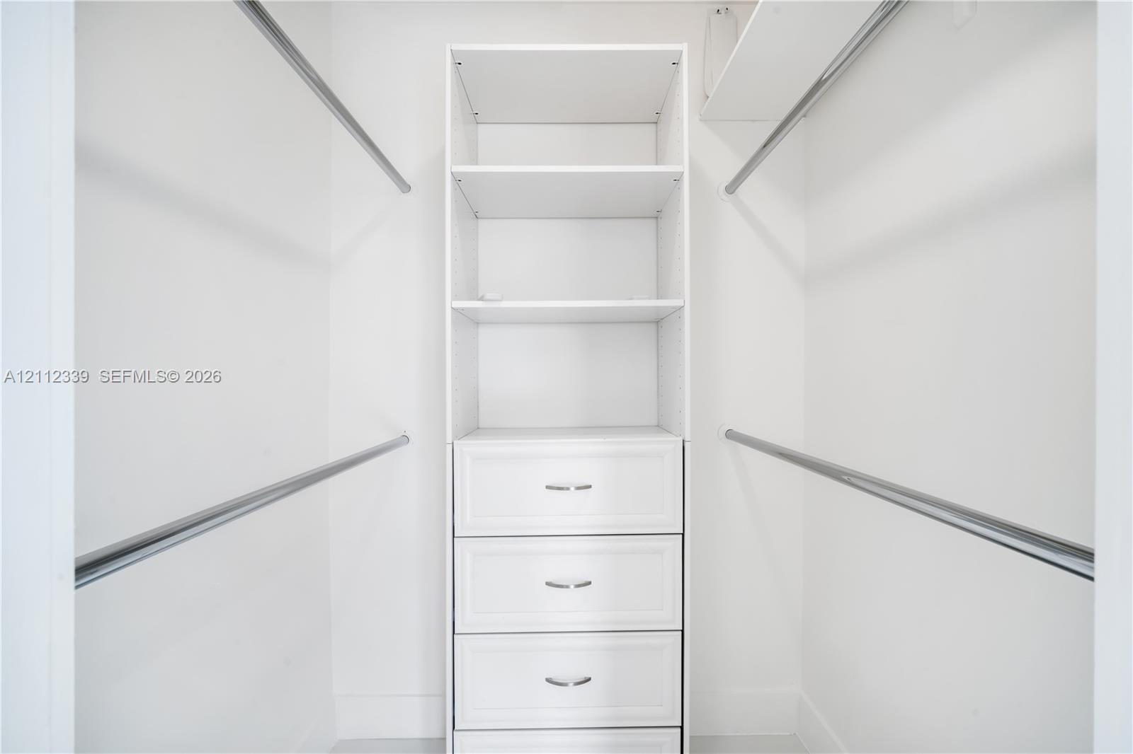 Custom walk-in closet featuring white built-in shelving, a four-drawer dresser unit with metallic pulls, and dual-level hanging rods