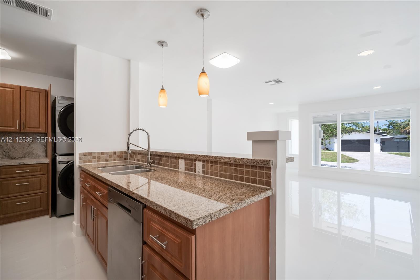 Kitchen featuring granite countertops, tile backsplash, stainless steel dishwasher, wood-finish cabinetry, and beautiful view to the living room and outdoors*