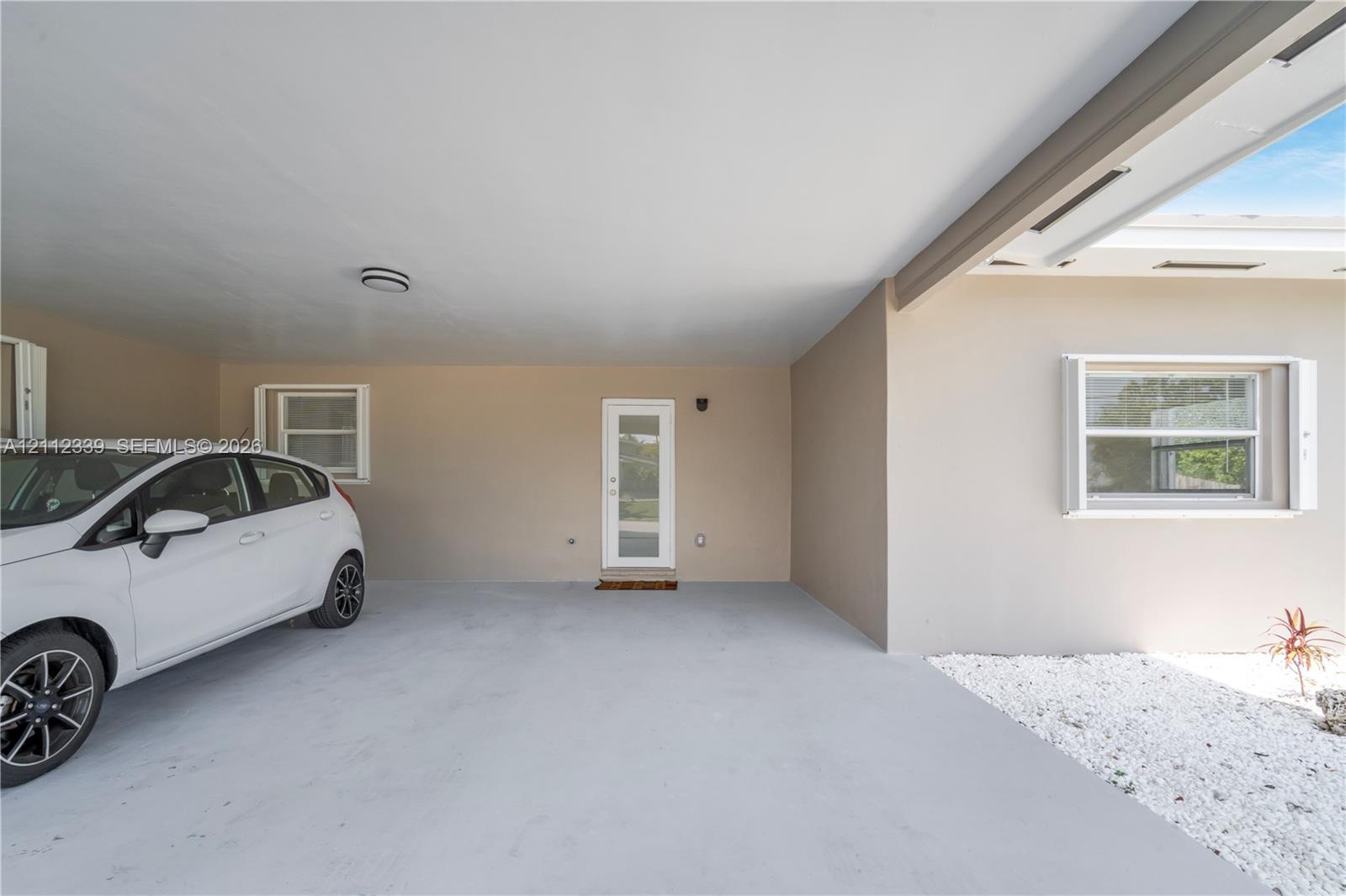 Covered carport for 1 car , featuring a smooth concrete floor, exterior wall lighting, and a glass-paneled entry door