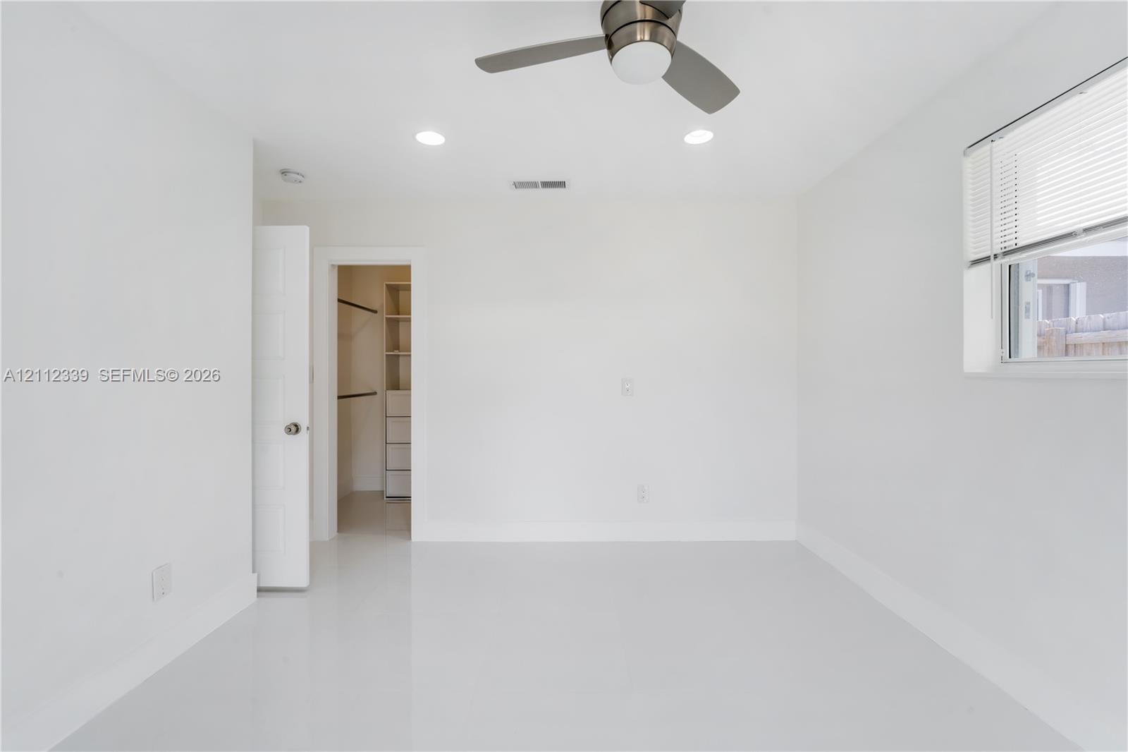 Interior space featuring smooth-finish flooring, recessed lighting, a brushed-nickel ceiling fan, and a walk-in closet with built-in shelving