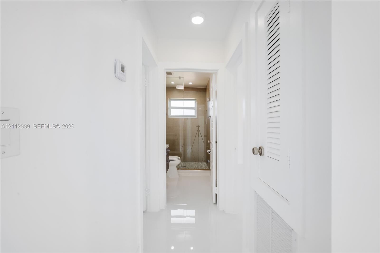 Hallway featuring crisp white walls, polished tile flooring, and built-in closet cabinetry with louvered doors