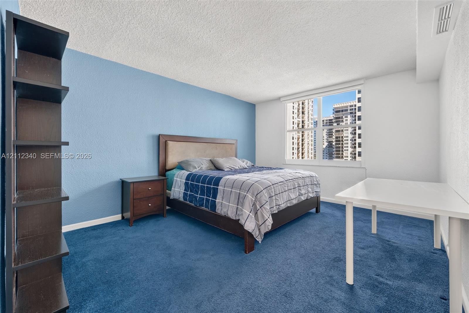 Bedroom featuring wall-to-wall carpeting, blue accent wall, and expansive window with urban cityscape
