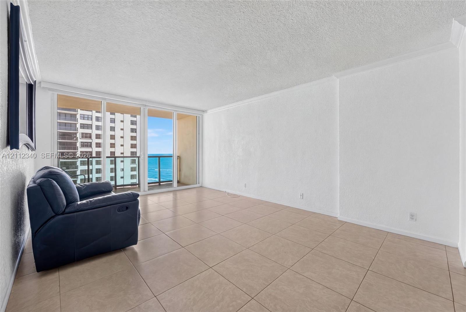 Open-concept room featuring oversized neutral floor tile, textured wall finishes, and floor-to-ceiling glass sliding doors opening to an exterior balcony