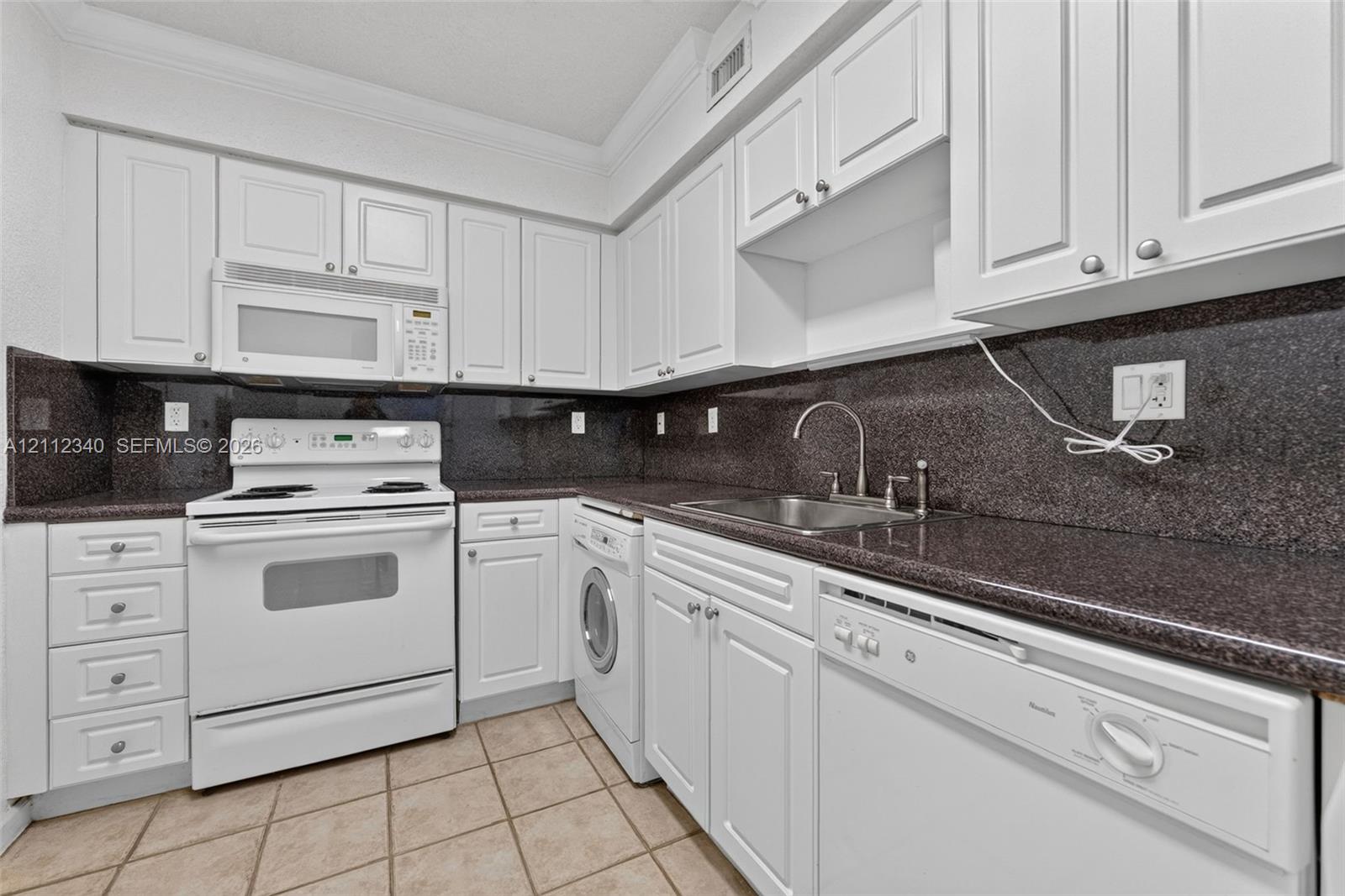 Kitchen featuring white cabinetry, dark stone-finish countertops, stainless steel sink with gooseneck faucet, built-in white appliances, and tile flooring Kitchen featuring white cabinetry, dark stone-finish countertops, stainless steel sink with gooseneck faucet, built-in white appliances, and tile flooring