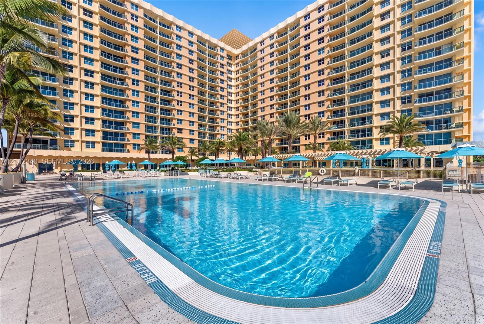 Resort-style swimming pool featuring tile decking, built-in metal handrails, and a dedicated perimeter lap lane, situated within a multi-story high-rise complex