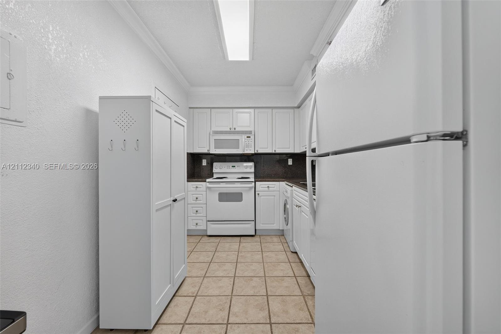 Kitchen featuring white cabinetry, tile flooring, integrated white appliances, and linear ceiling lighting Kitchen featuring white cabinetry, tile flooring, integrated white appliances, and linear ceiling lighting