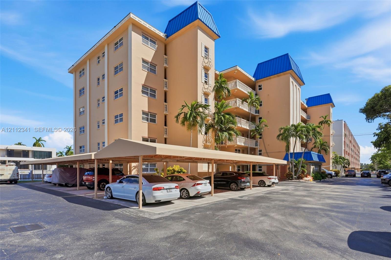 Multi-story residential building featuring blue metal roof accents, recessed private balconies, and a covered parking structure