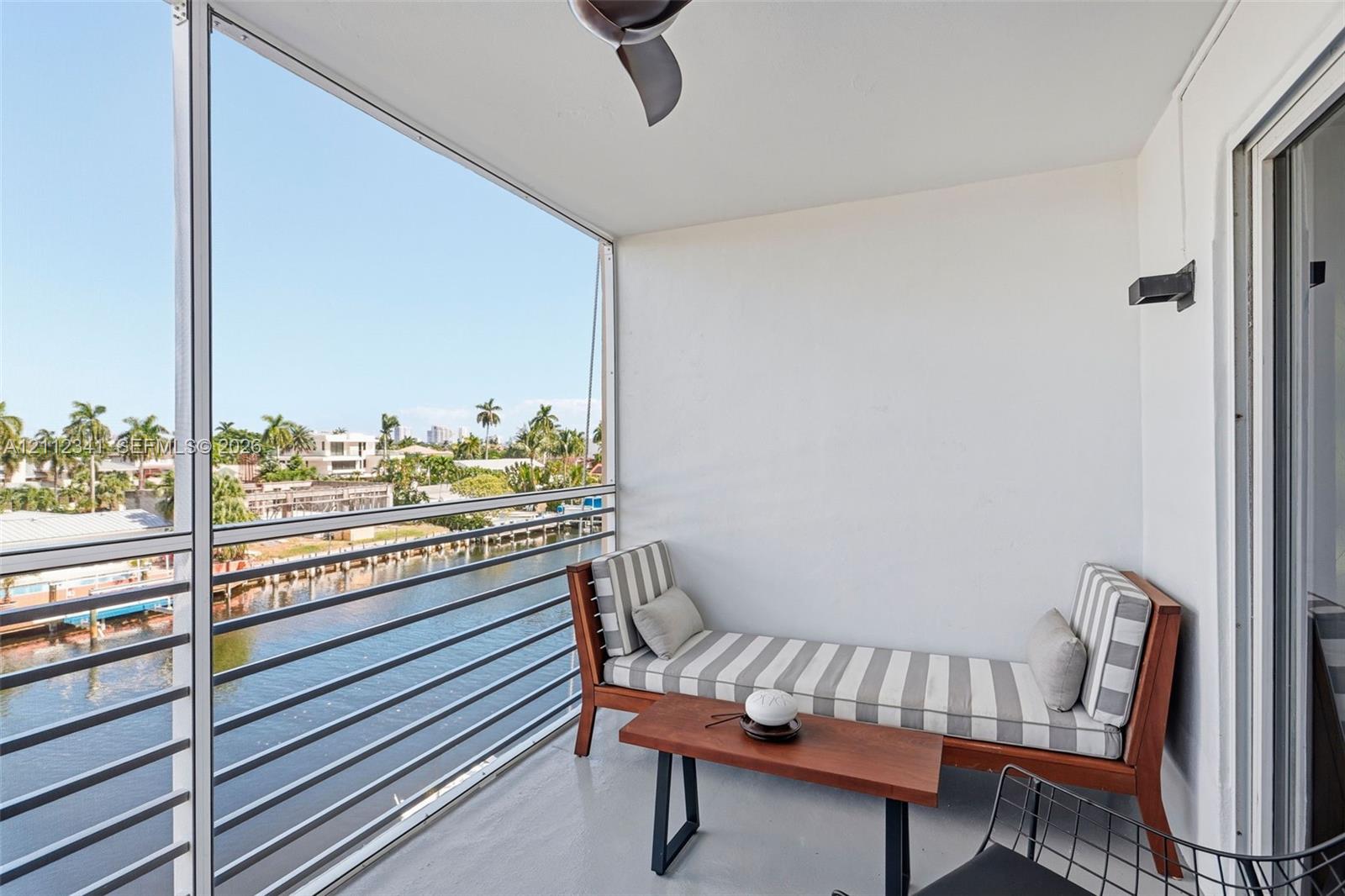 Screened balcony featuring a metal railing, ceiling fan, and wall-mounted light fixture