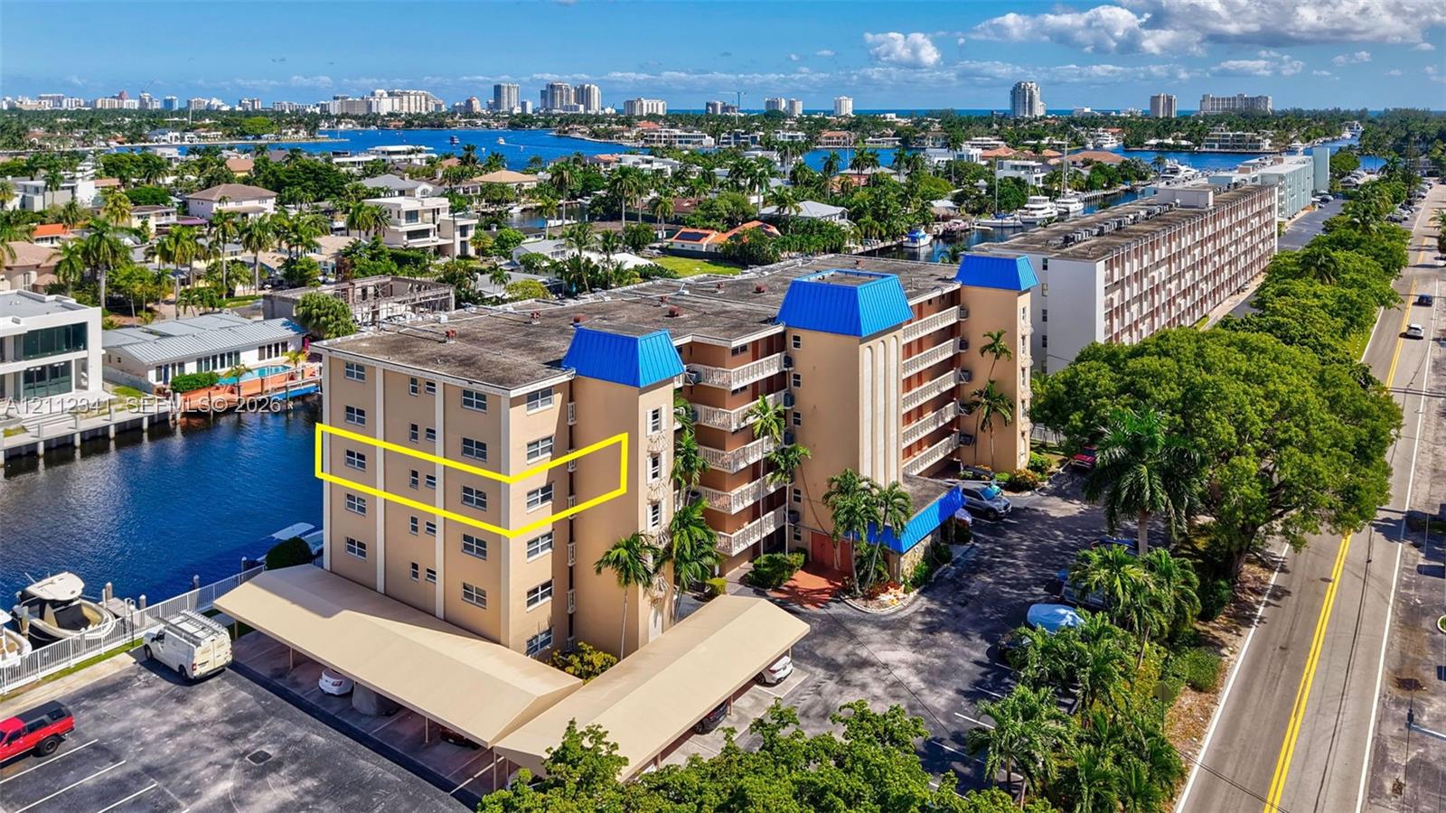 Multi-story residential building featuring covered parking, blue mansard roof accents, canal-side positioning, and exterior balconies