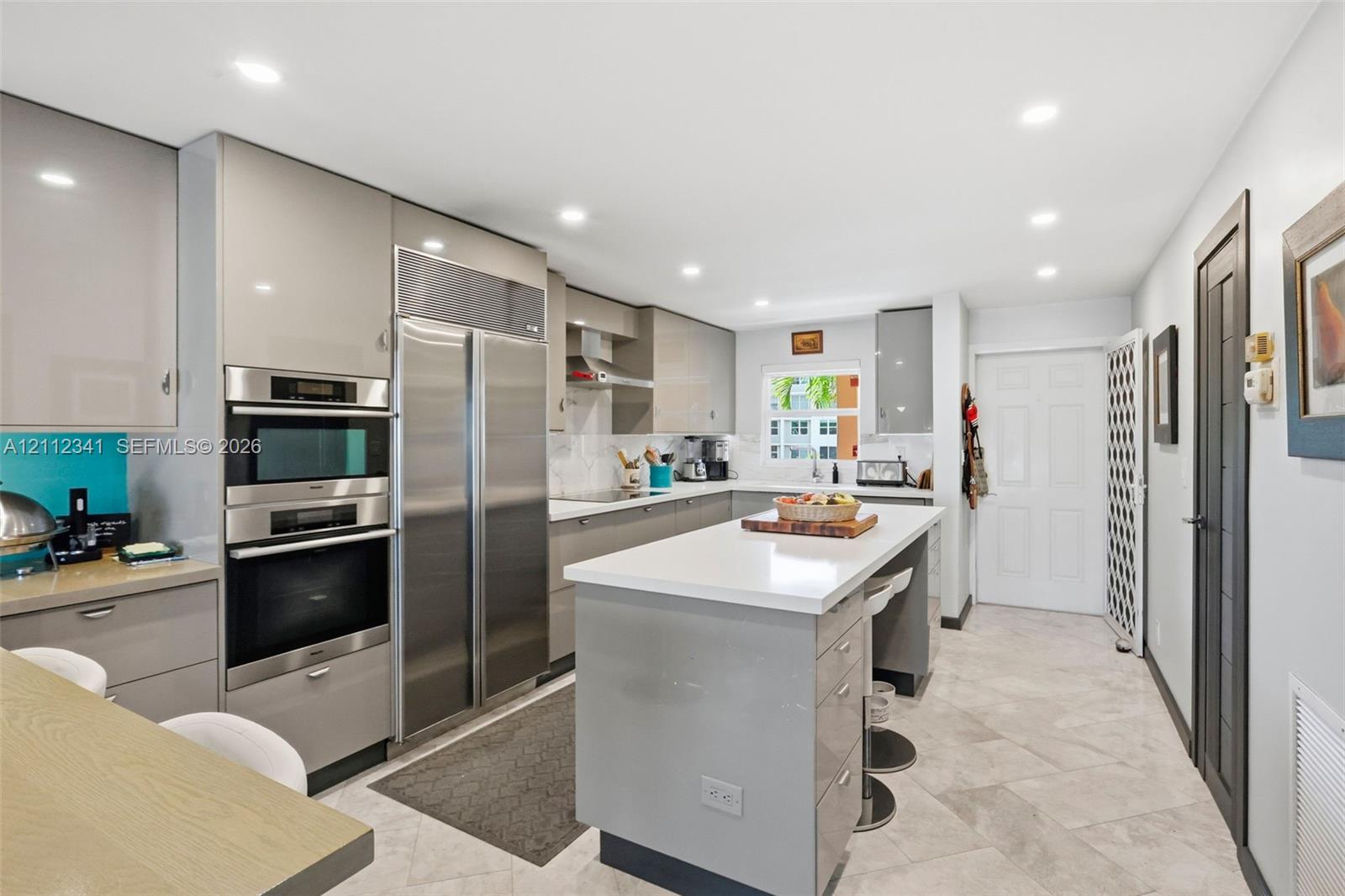 Kitchen featuring high-gloss cabinetry, stone countertops, a central island with integrated seating, stainless steel double-wall ovens, and large-format tile flooring