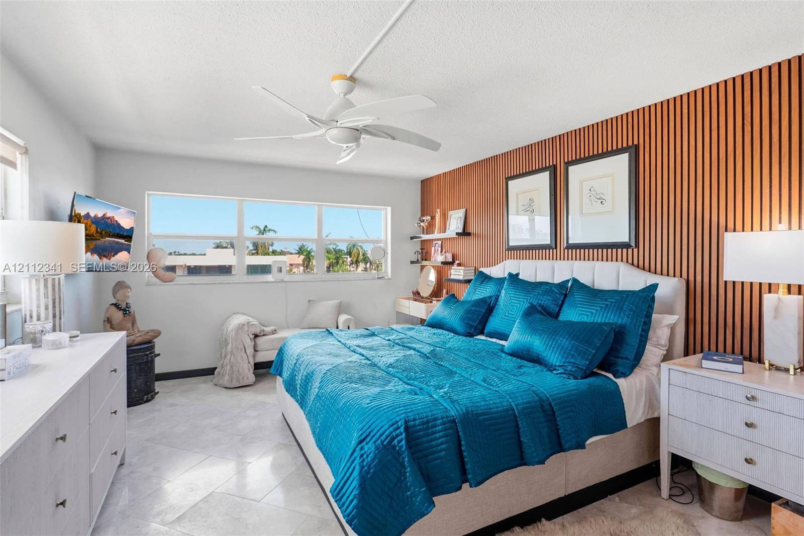 Bedroom featuring a floor-to-ceiling wood slat accent wall, tile flooring, large horizontal window, and a ceiling fan
