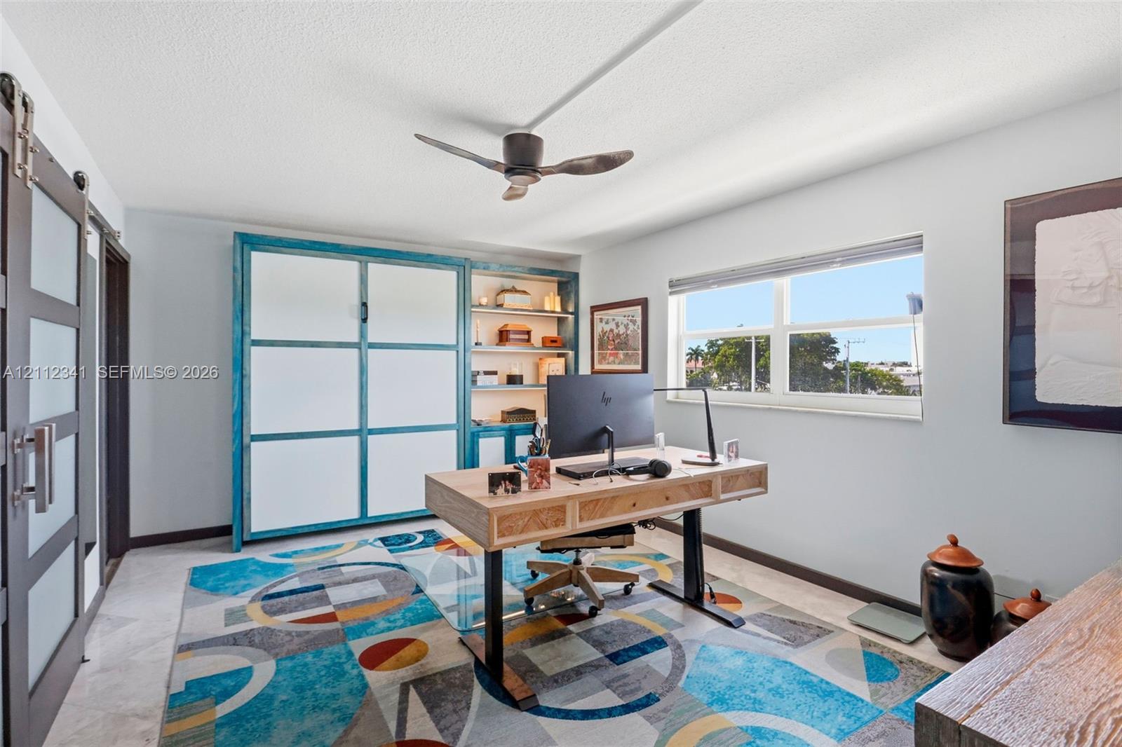 Built-in cabinetry with integrated shelving, sliding glass-panel door, ceiling fan with matte finish, and horizontal window