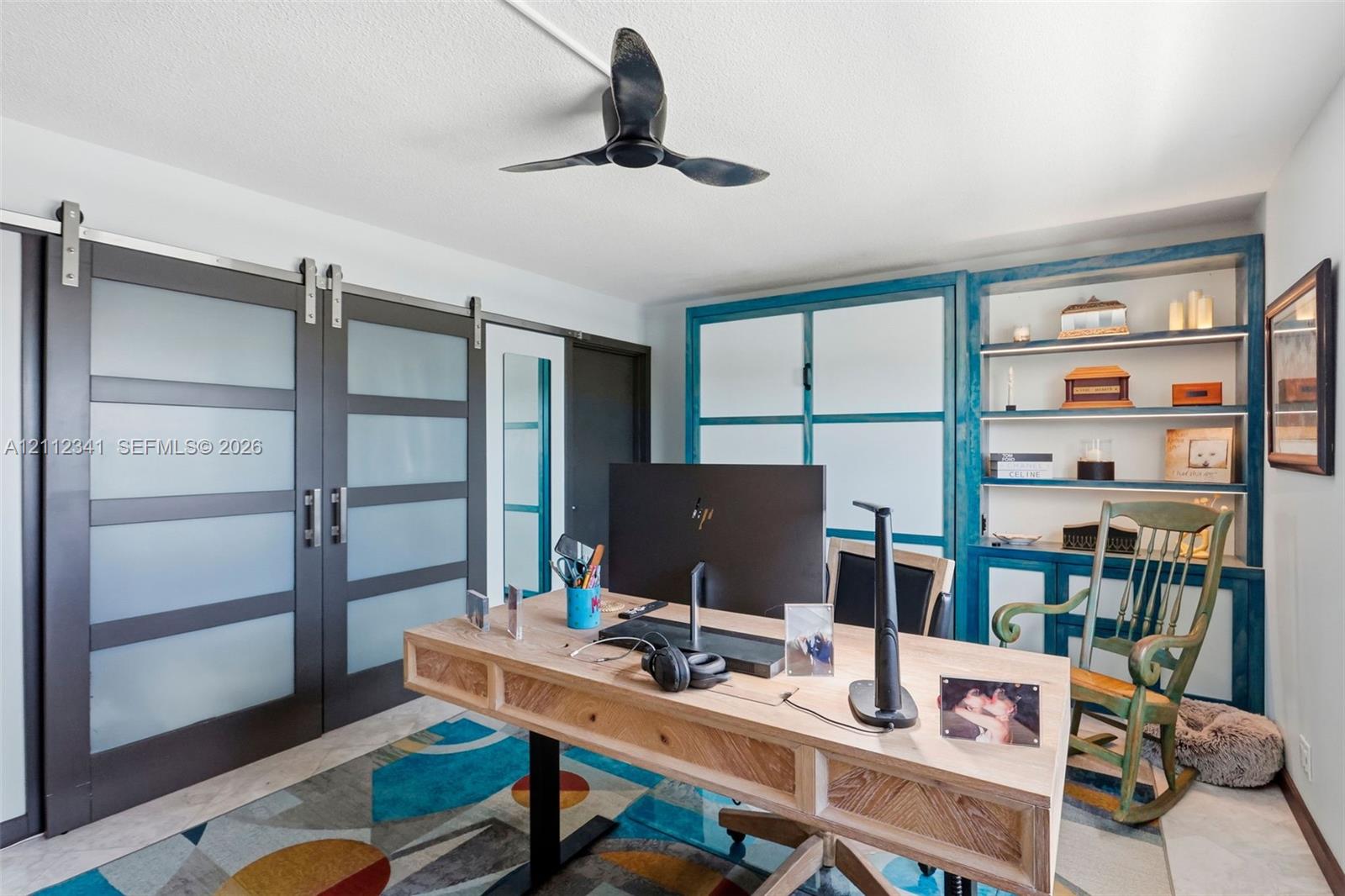 Dual sliding barn doors with frosted glass panels, built-in floor-to-ceiling cabinetry with open shelving, and a matte black three-blade ceiling fan