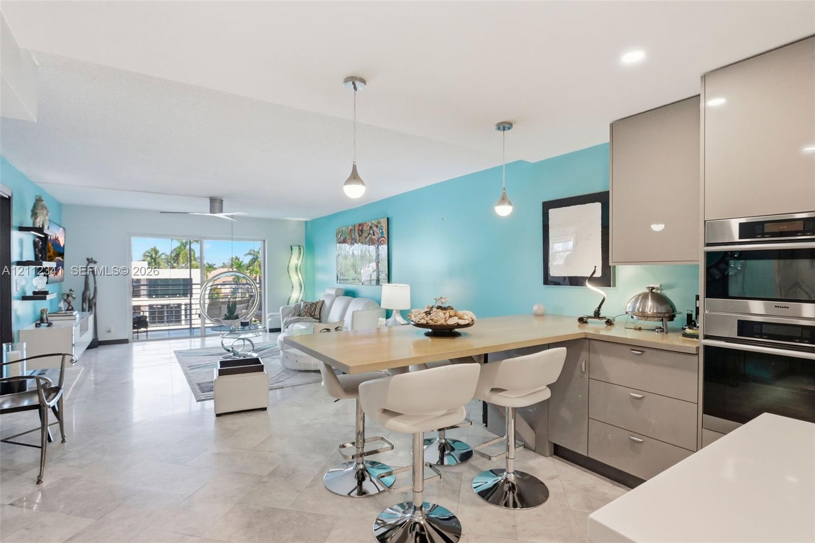 Open-concept kitchen featuring high-gloss cabinetry, stone-finish flooring, built-in stainless steel double wall ovens, and a peninsula with integrated breakfast bar seating