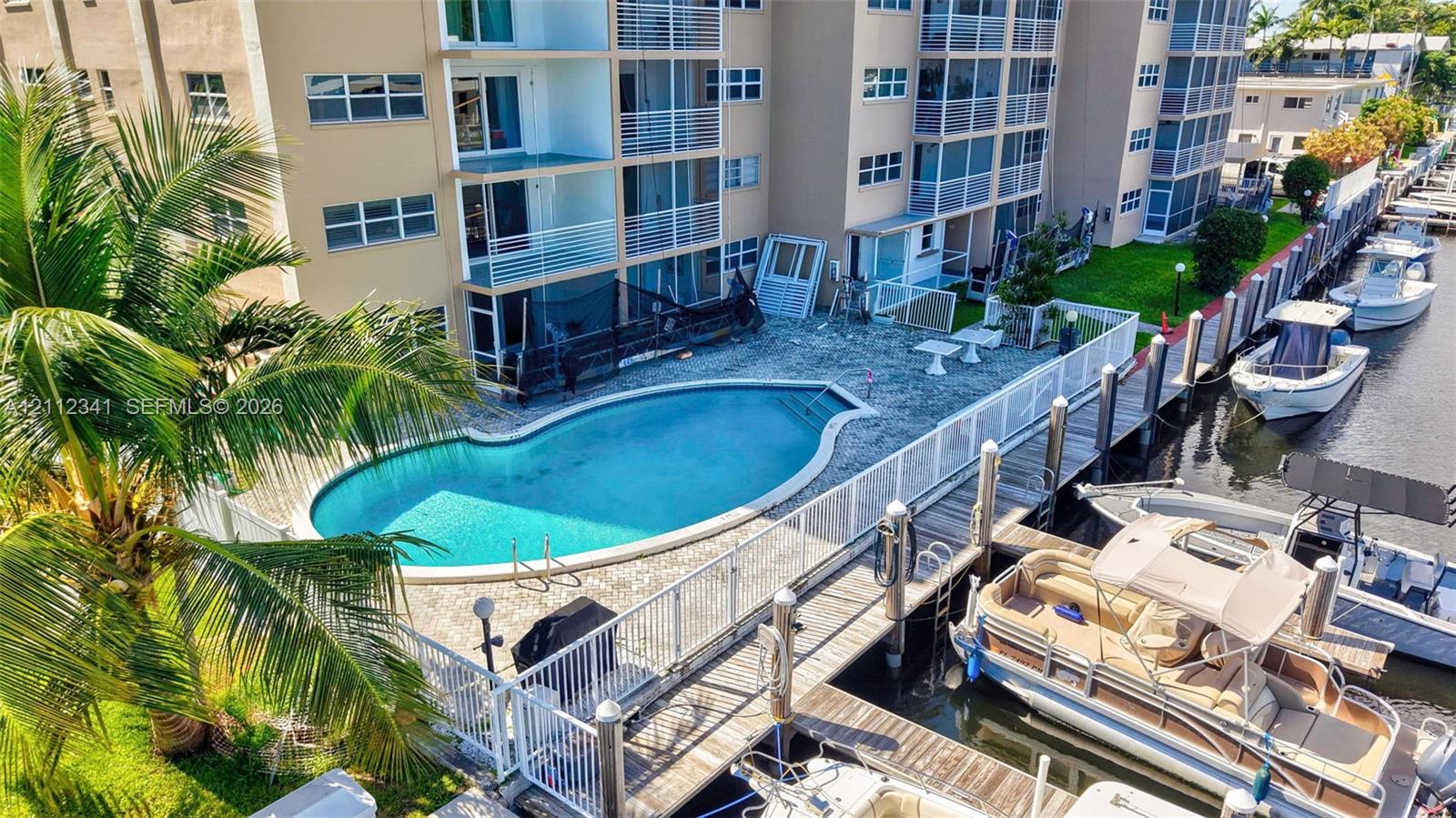 Exterior grounds featuring an in-ground swimming pool, stone-paver pool deck, white perimeter fencing, and private wooden boat docks along a canal