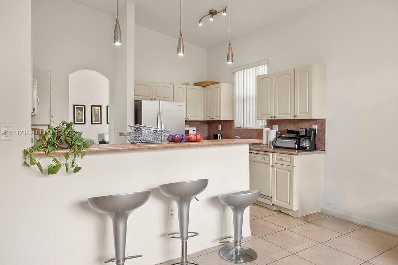 Kitchen featuring an elevated breakfast bar with stone-finish surfacing, light-toned cabinetry, ceramic tile flooring, and multi-pendant lighting