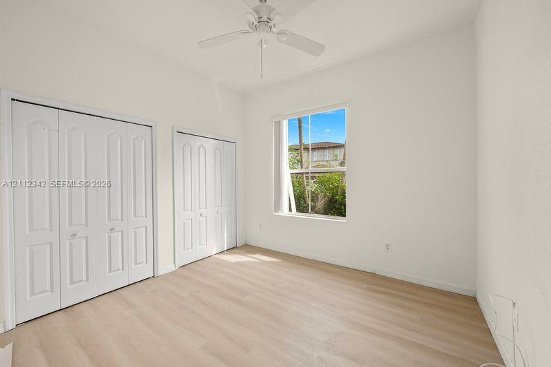 Room featuring wood-finish flooring, dual bi-fold door closets, a single-hung window, and a ceiling fan