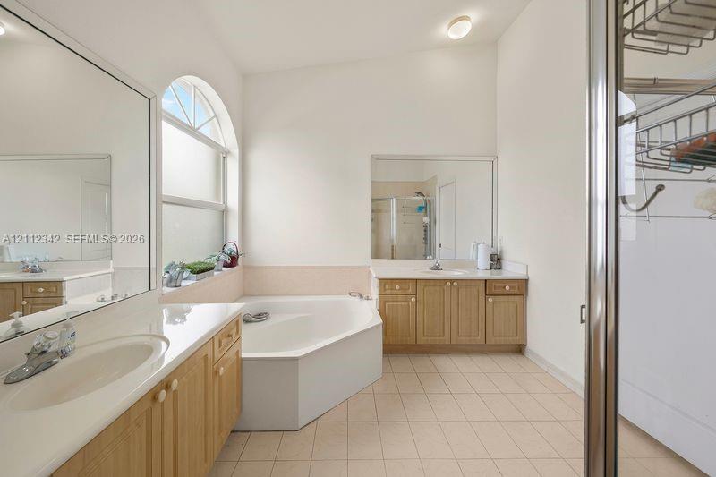 Bathroom featuring dual wooden vanities with white countertops, a deep corner soaking tub, a large arched window, and full-length mirrors